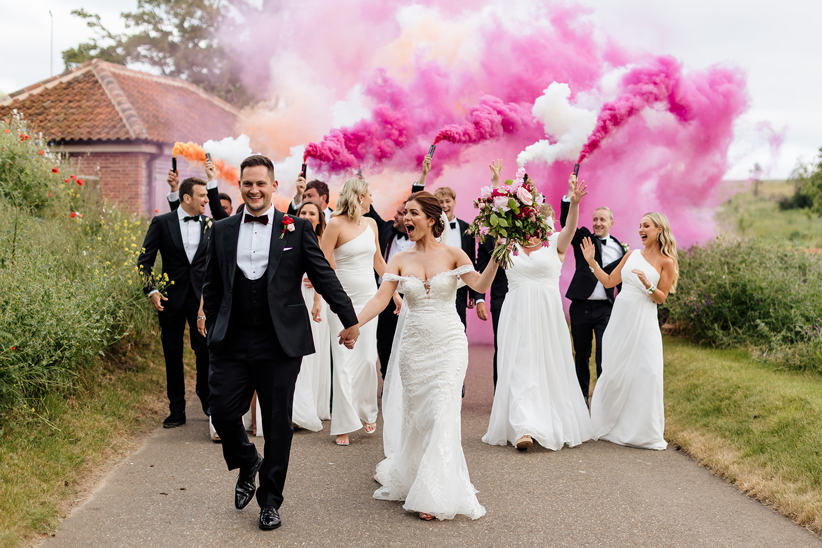 Bride and groom with wedding party holding pink and white flares. 