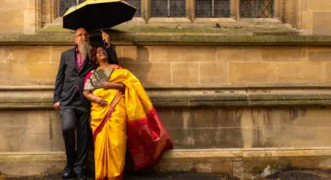 Indian couple looking up and smiling outside with groom holding an umbrella