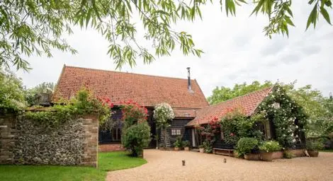 Black barn with red and white flowers in shrubs.