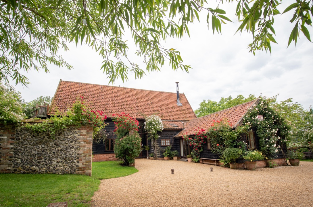 Black barn with red and white flowers in shrubs. 