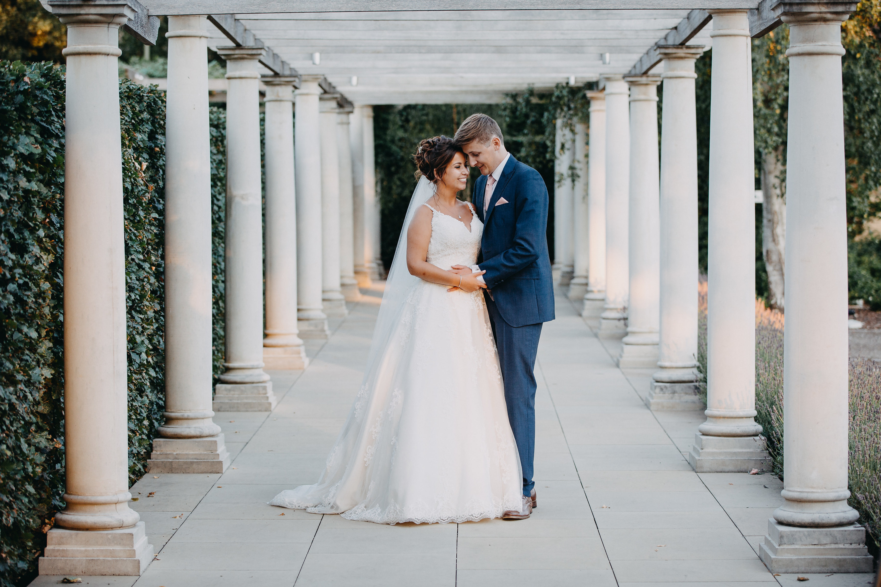 Bride and groom holding hands outside with pillars beside them.