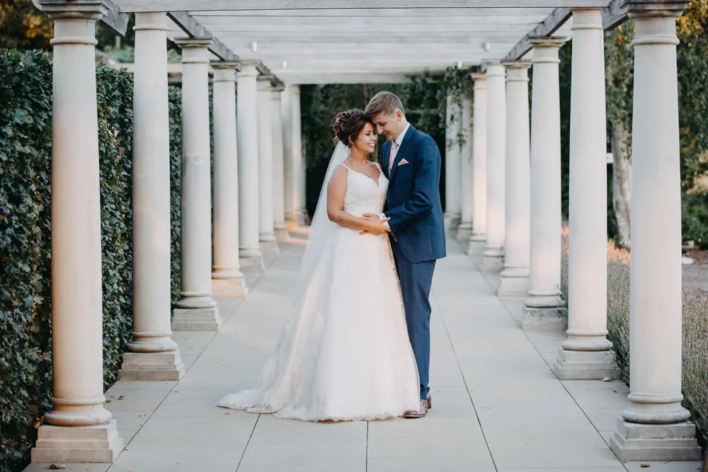Bride and groom holding hands outside with pillars beside them.