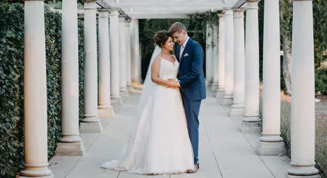 Bride and groom holding hands outside with pillars beside them.