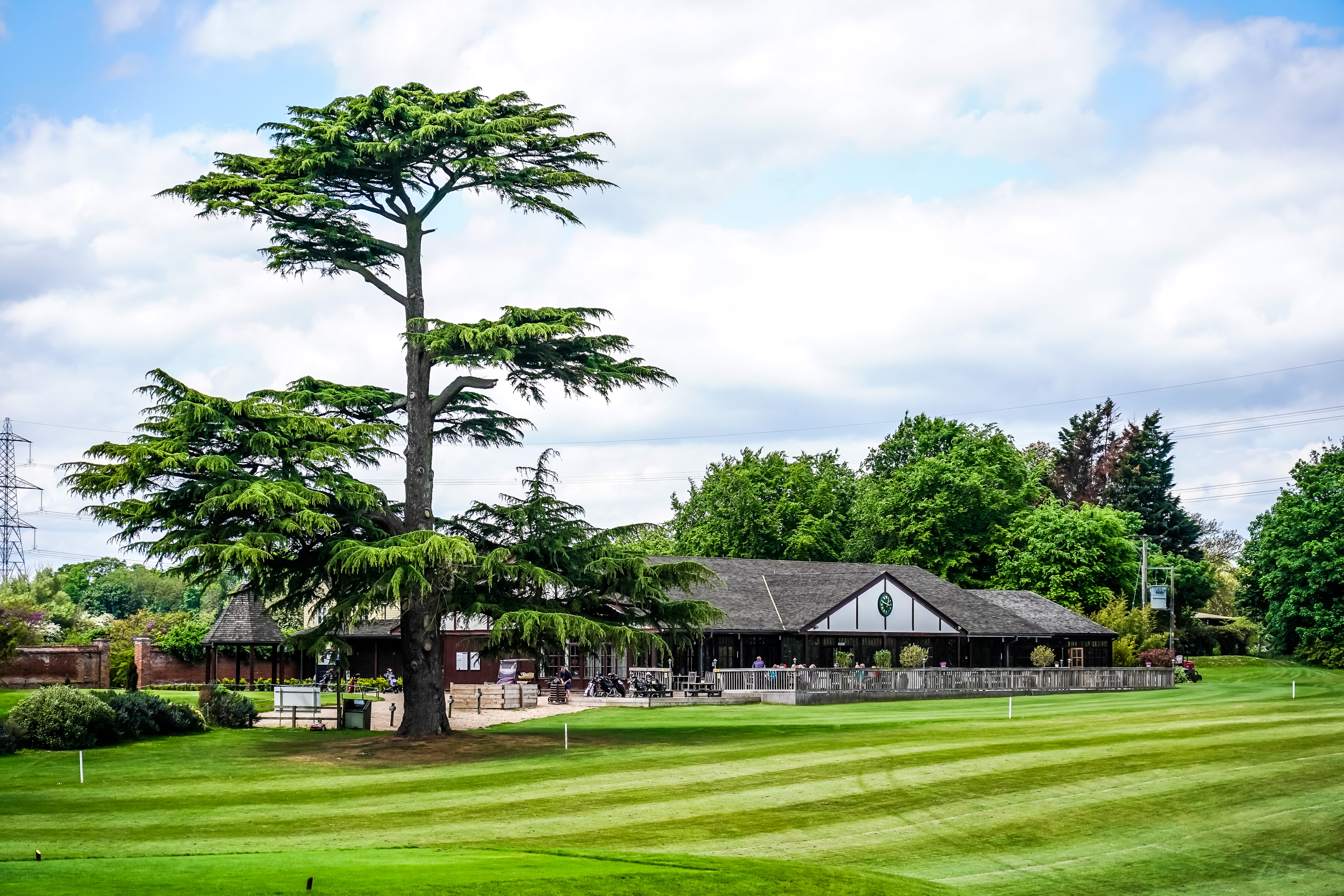 Outside of Hintlesham Golf Club with neatly lined grass and tables outside on a patio.