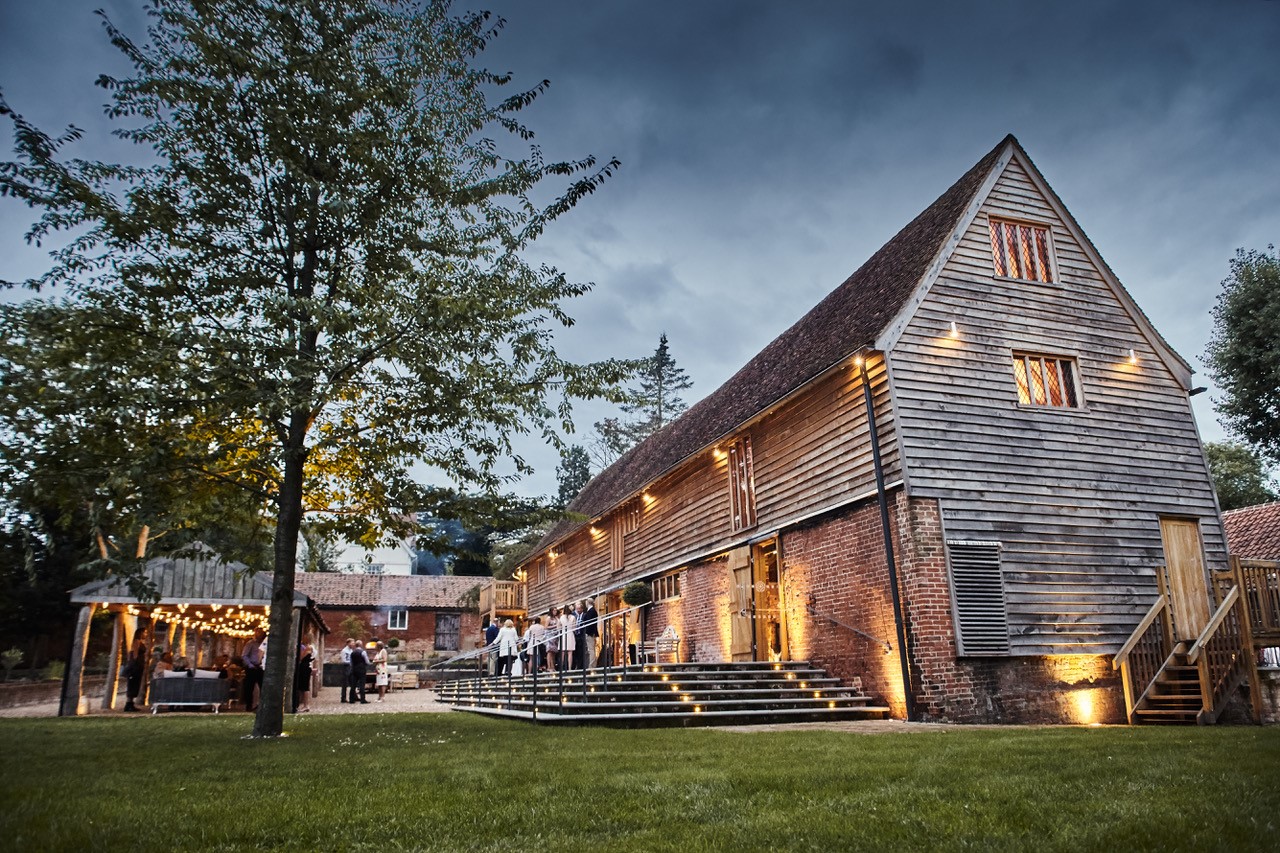 Outside Tudor Barn with wedding guests standing in courtyard with fairy lights on.