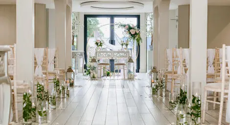 Chairs facing towards a flower arch. Flowers in glass vases and petals on the edge of the aisle.