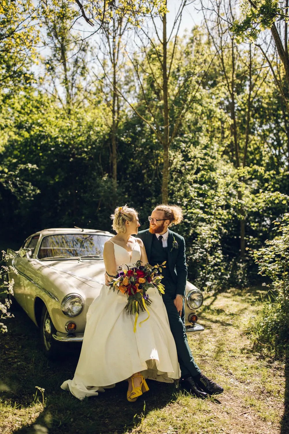 Bride and groom sitting on car looking at each other happily. Photo by Chloe Lee Photo