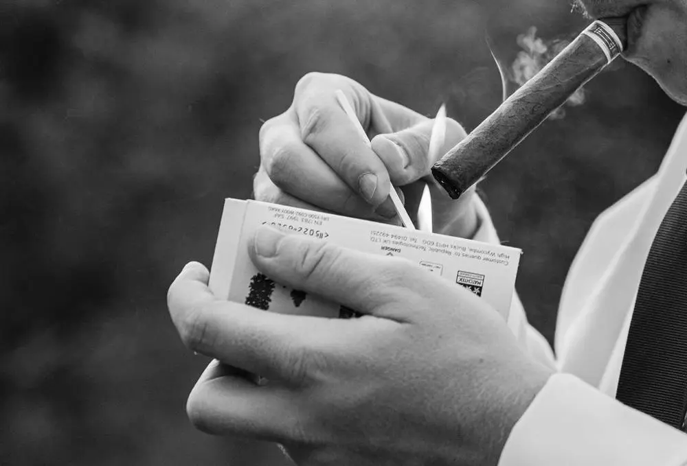 black and white image hands striking match to light cigar