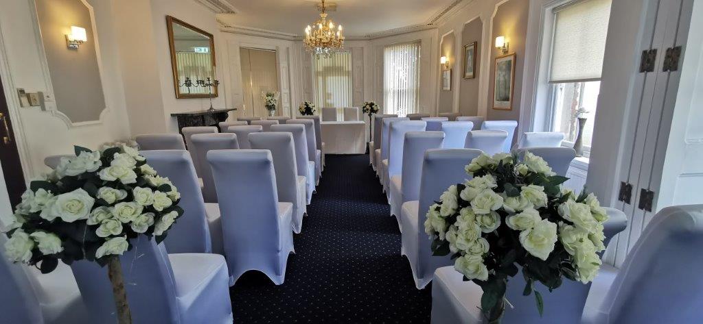 Chairs with white covers facing forwards. White roses at the top of the wedding aisle. 