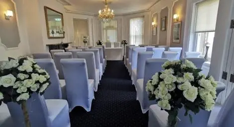 Chairs with white covers facing forwards. White roses at the top of the wedding aisle.