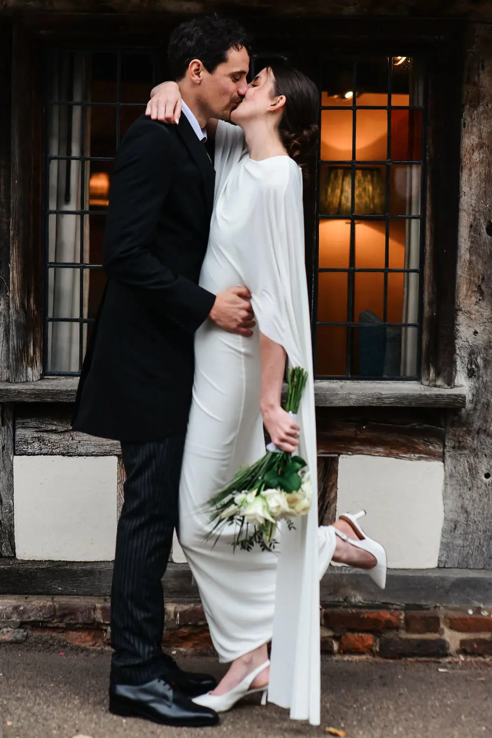Bride and groom kissing outside Tudor building