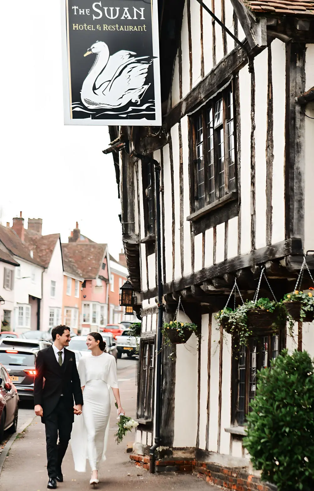 Bride and groom walking in front of Tudor building in Lavenham Suffolk