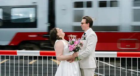 Bride and groom standing at level crossing with train whooshing past
