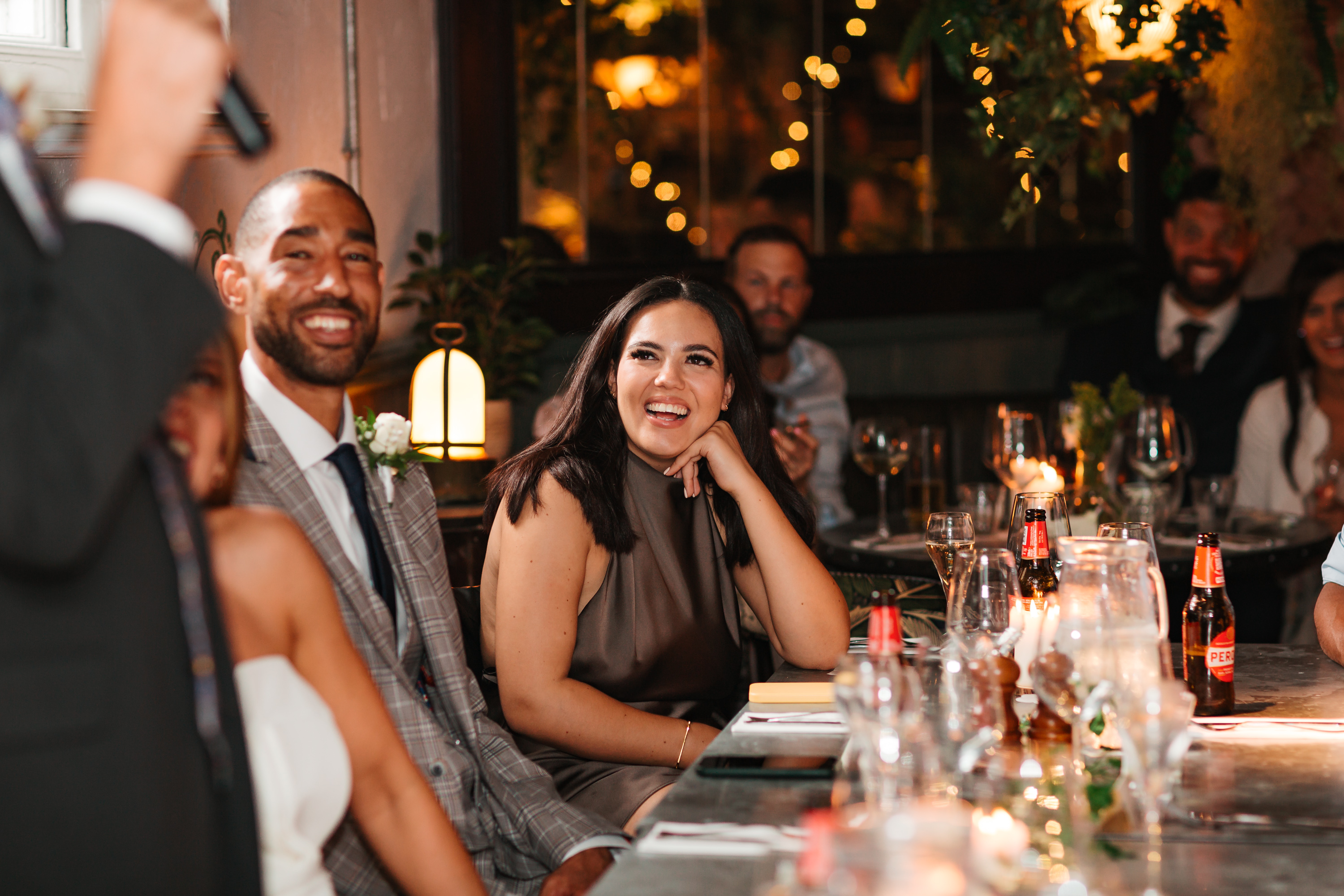 Wedding guests smiling and listening to a best man speech.
