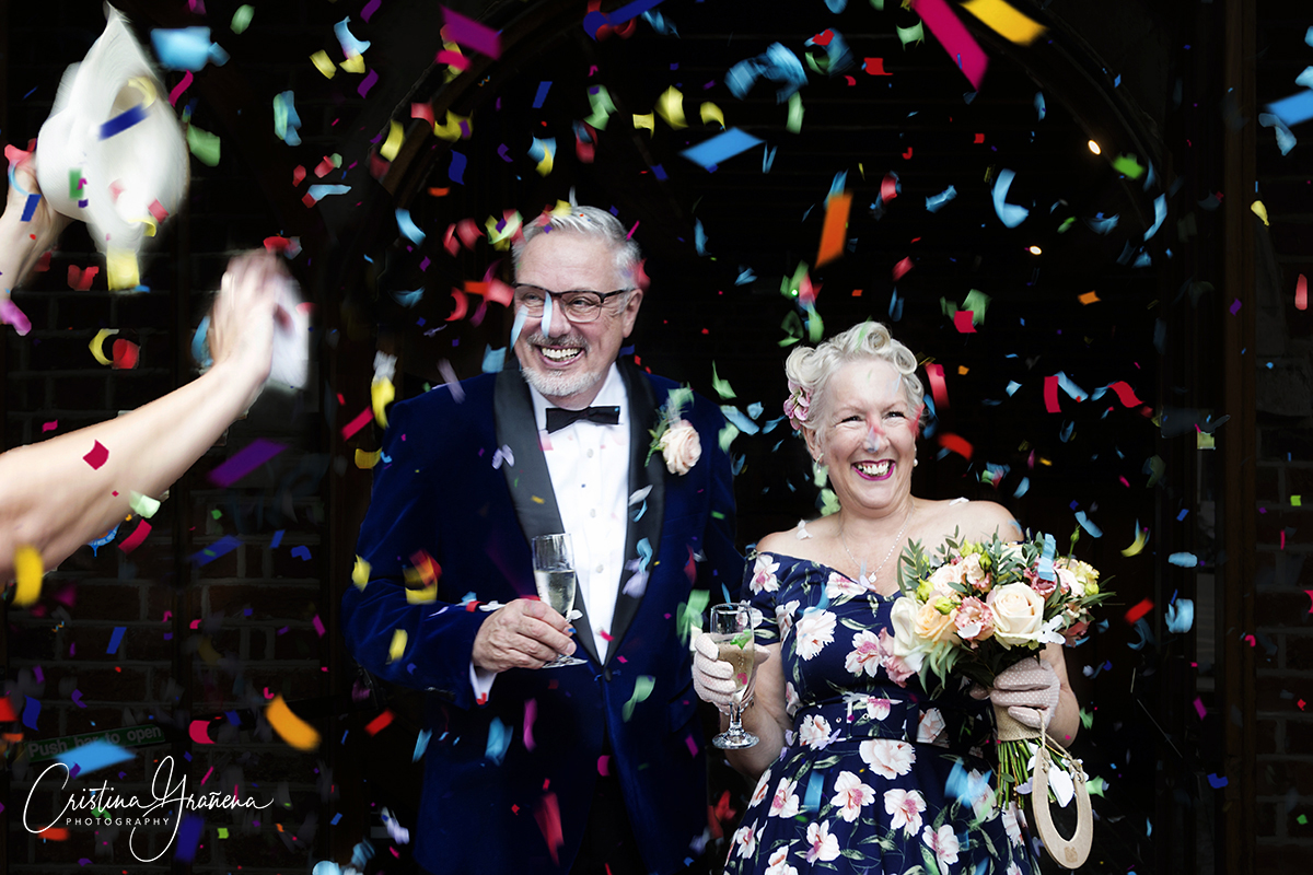 Older couple on their wedding day in a shower of colourful confetti with champagne