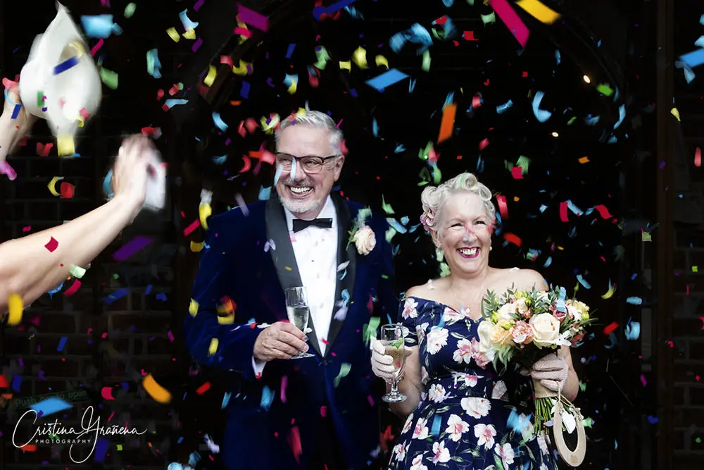 Older couple on their wedding day in a shower of colourful confetti with champagne