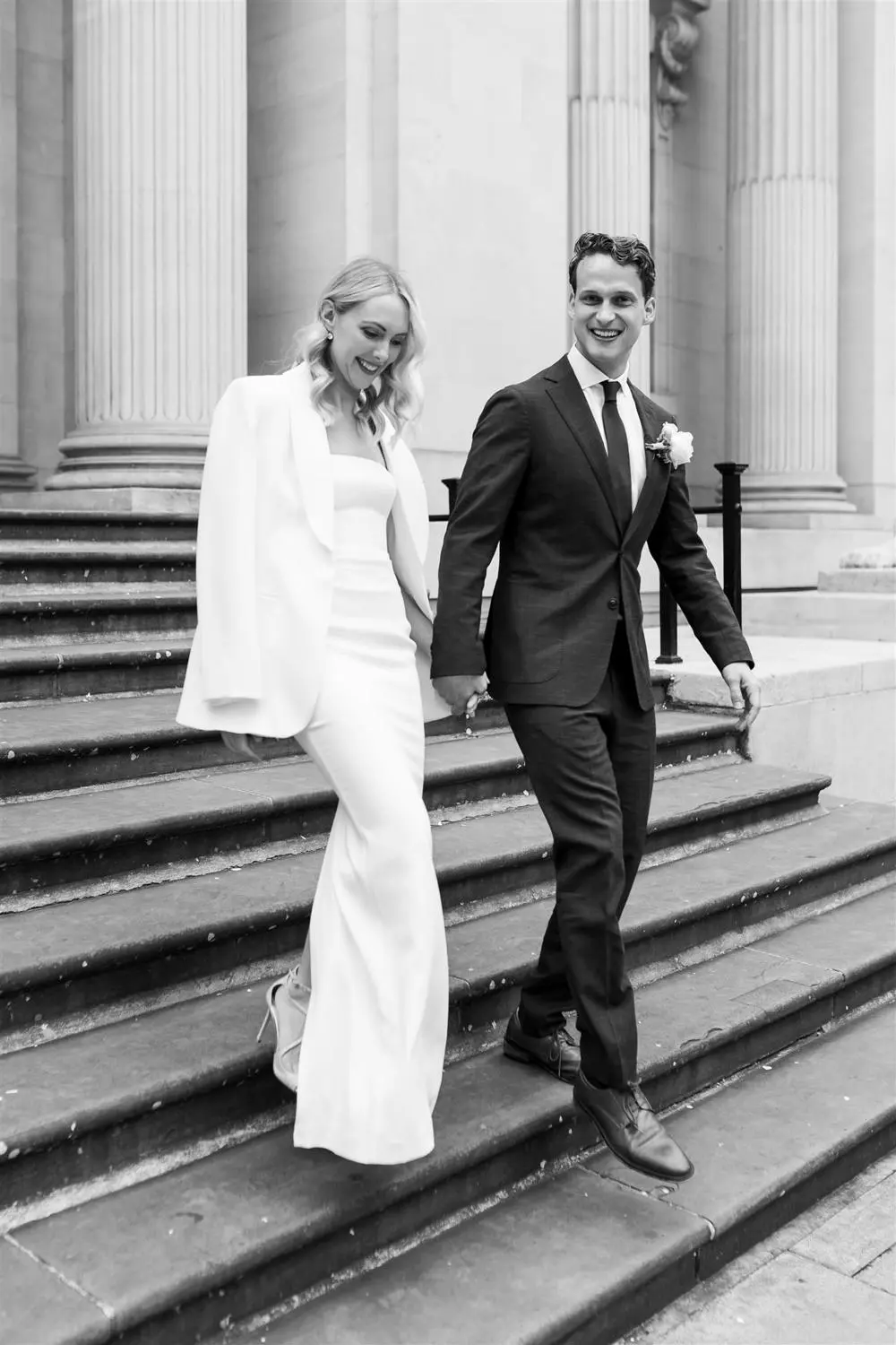 Black and white photo of chic bride and groom walking down some stairs