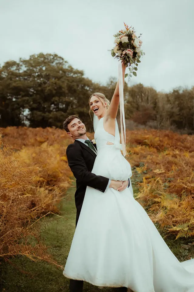 Groom lifting bride up in autumn countryside setting