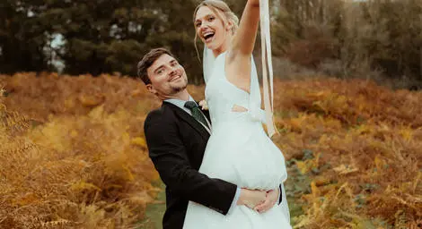Groom lifting bride up in autumn countryside setting