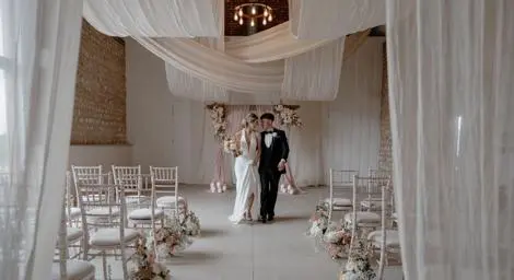 Bride and Groom in beautifully decorated ceremony room with white chairs, white flowers and white drapery
