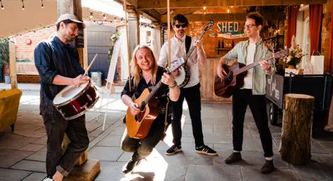 Folksy four piece band with three guitars and one drum playing in barn
