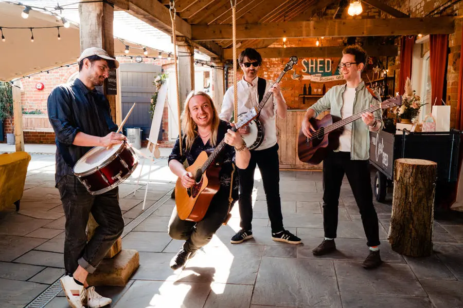 Folksy four piece band with three guitars and one drum playing in barn