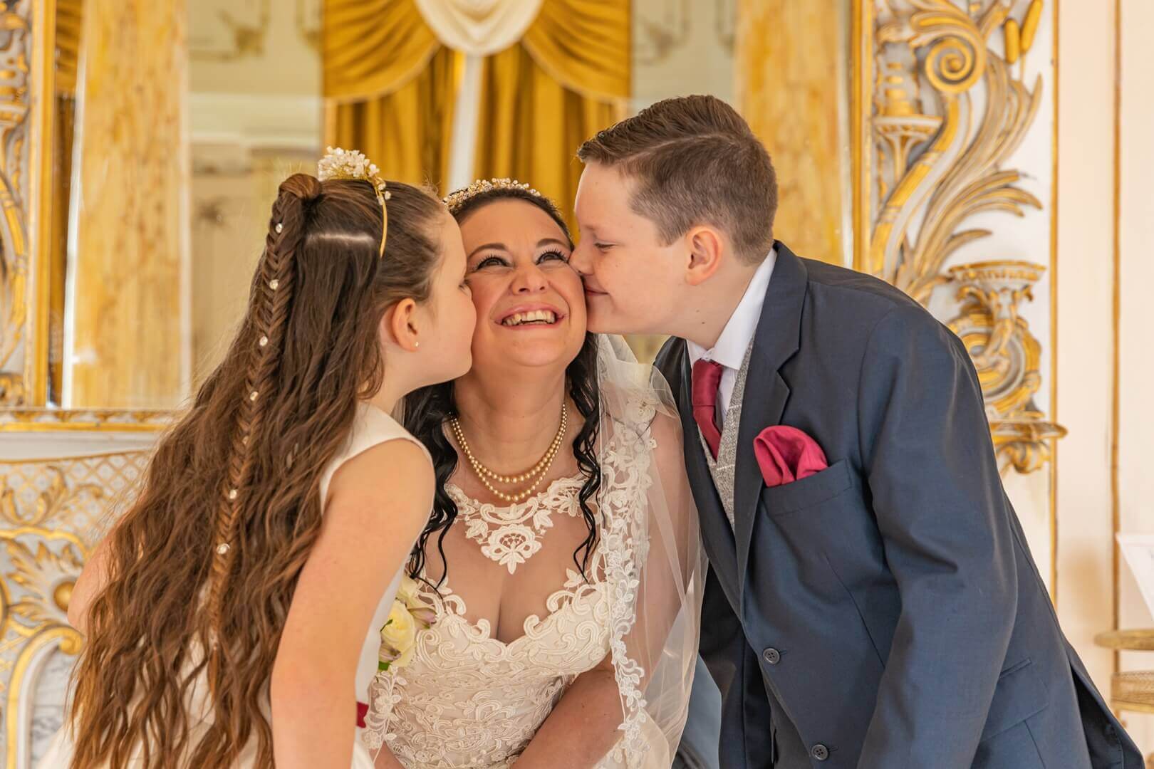 Boy and girl kissing their mum at her wedding