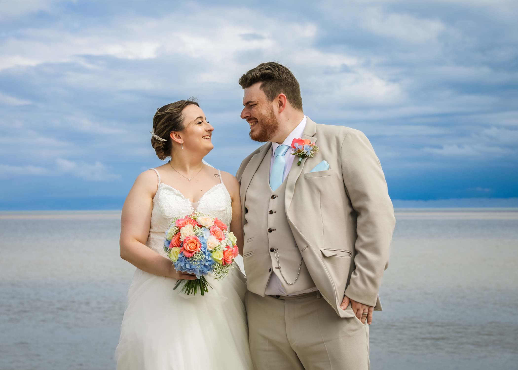 Bride and groom by the seaside smiling at each other