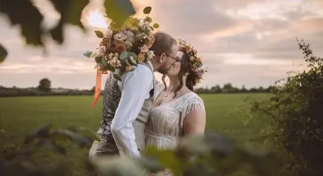 Bride and groom with beautiful flowers kissing in meadow