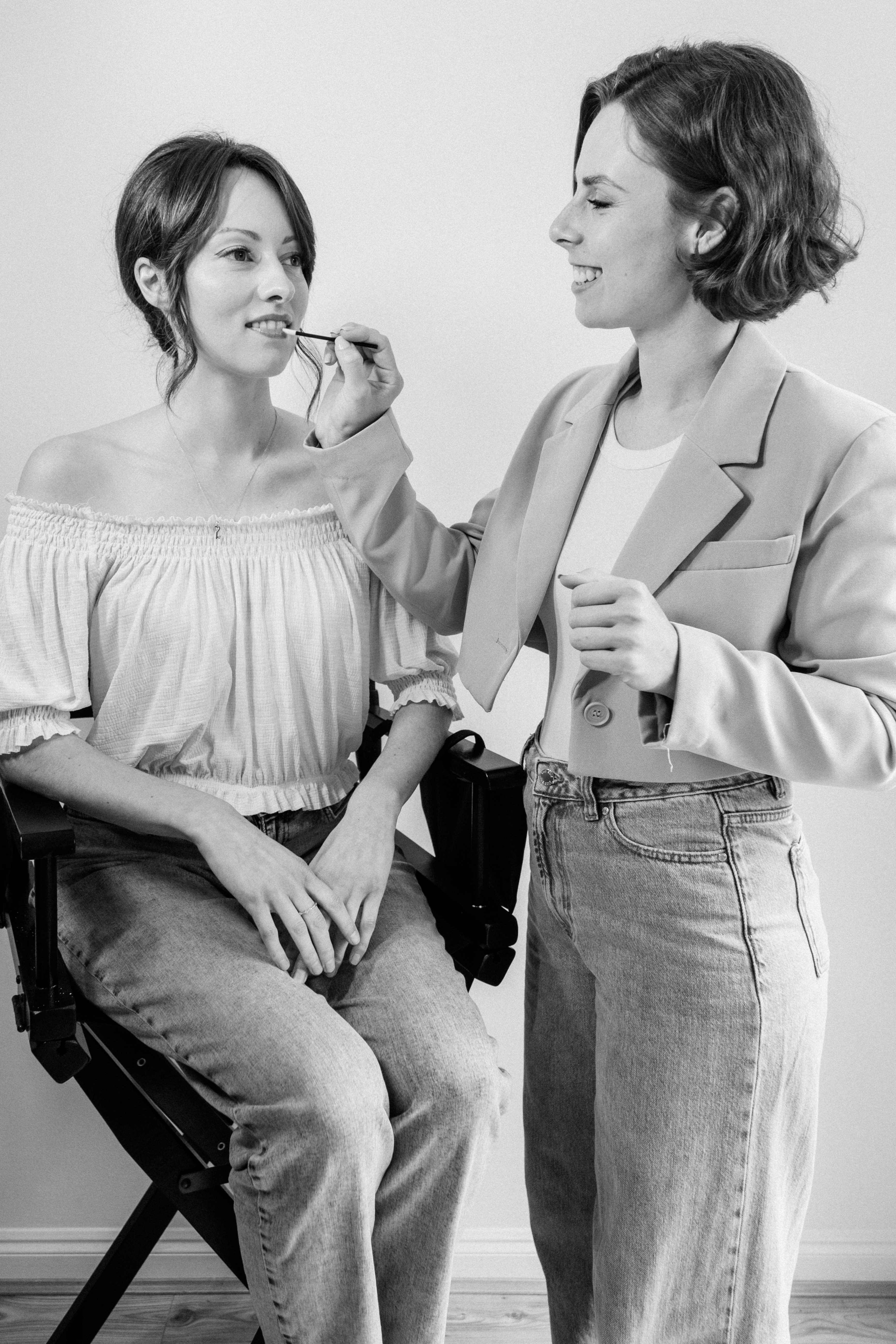 Make up artist applying lip gloss to a woman sitting in a chair