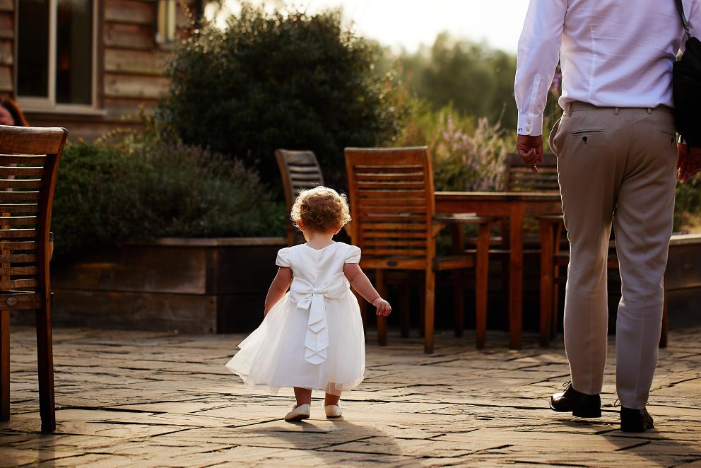 Little toddler girl in white dress at wedding walking with dad