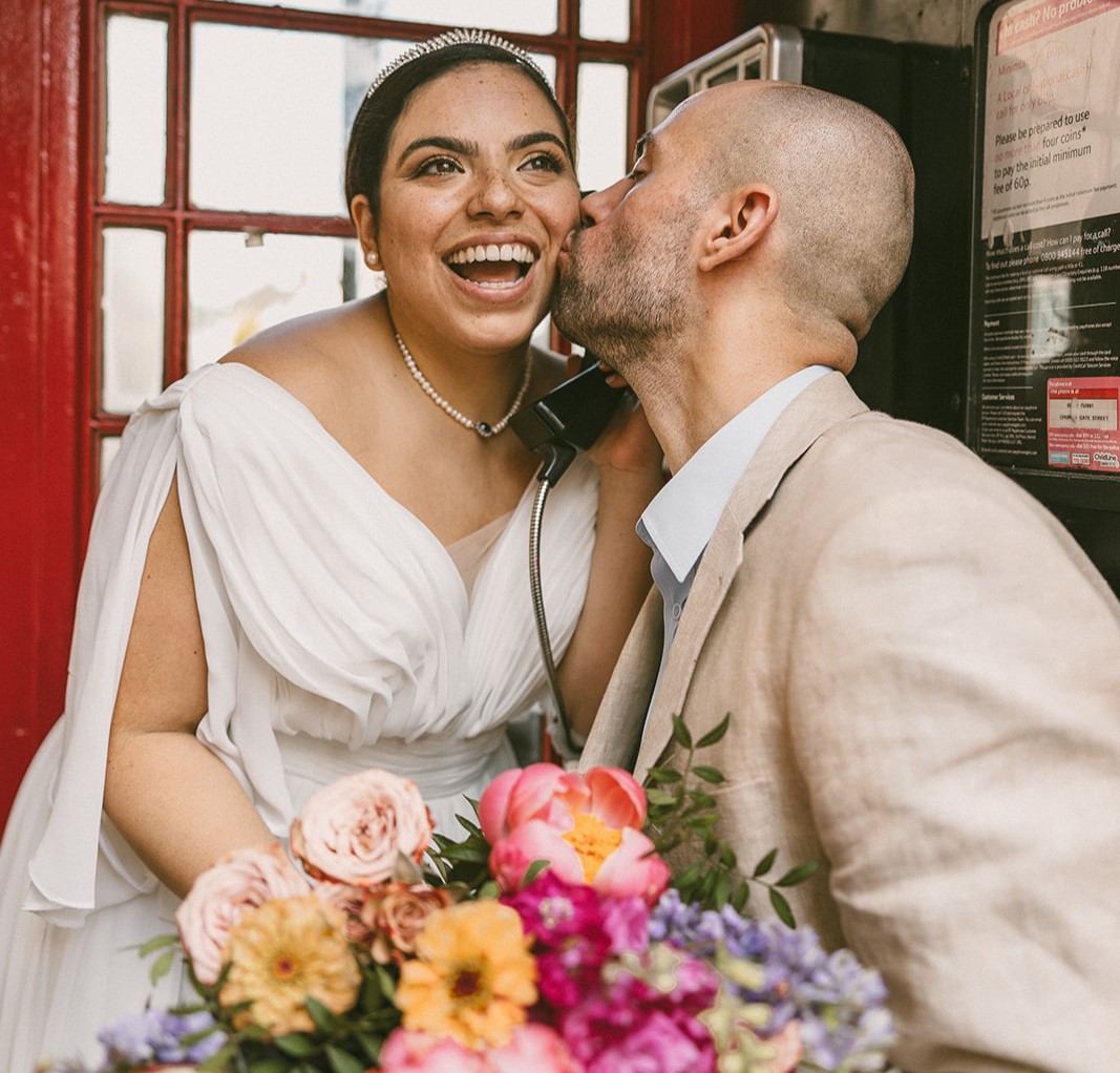 Groom kissing smiling bride in a phone booth