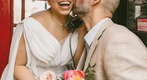 Groom kissing smiling bride in a phone booth