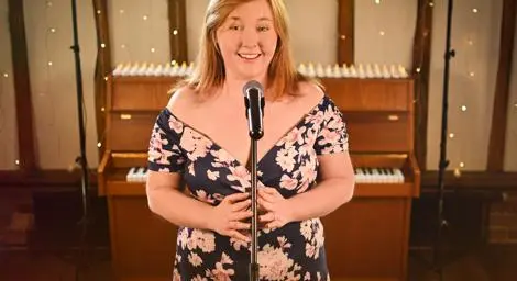 Naomi Collins Vocalist standing behind mic with a piano in the background