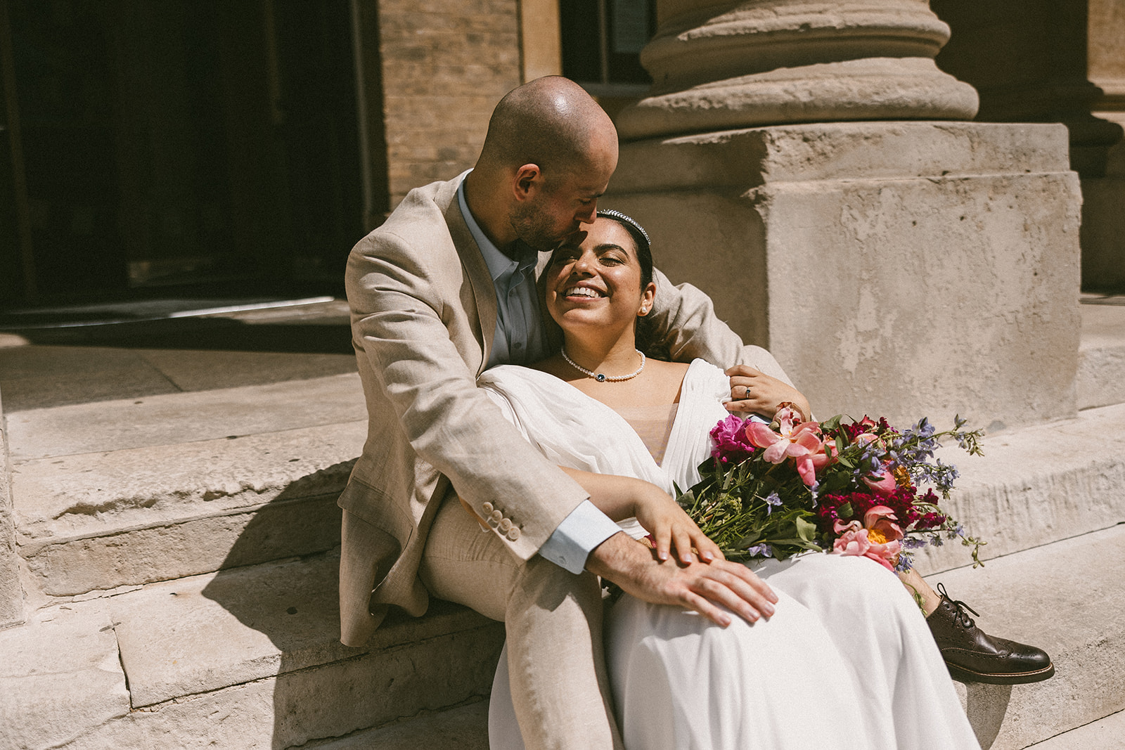 Bride and groom sitting in the sun on the steps of the Corn Exchange in Bury St Edmunds