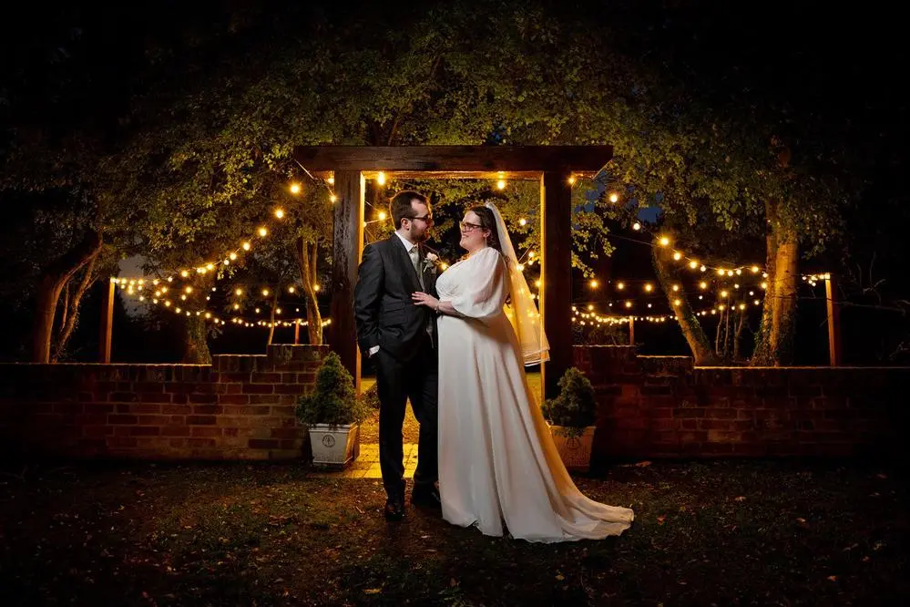 Bride and groom at night under a lit arbour