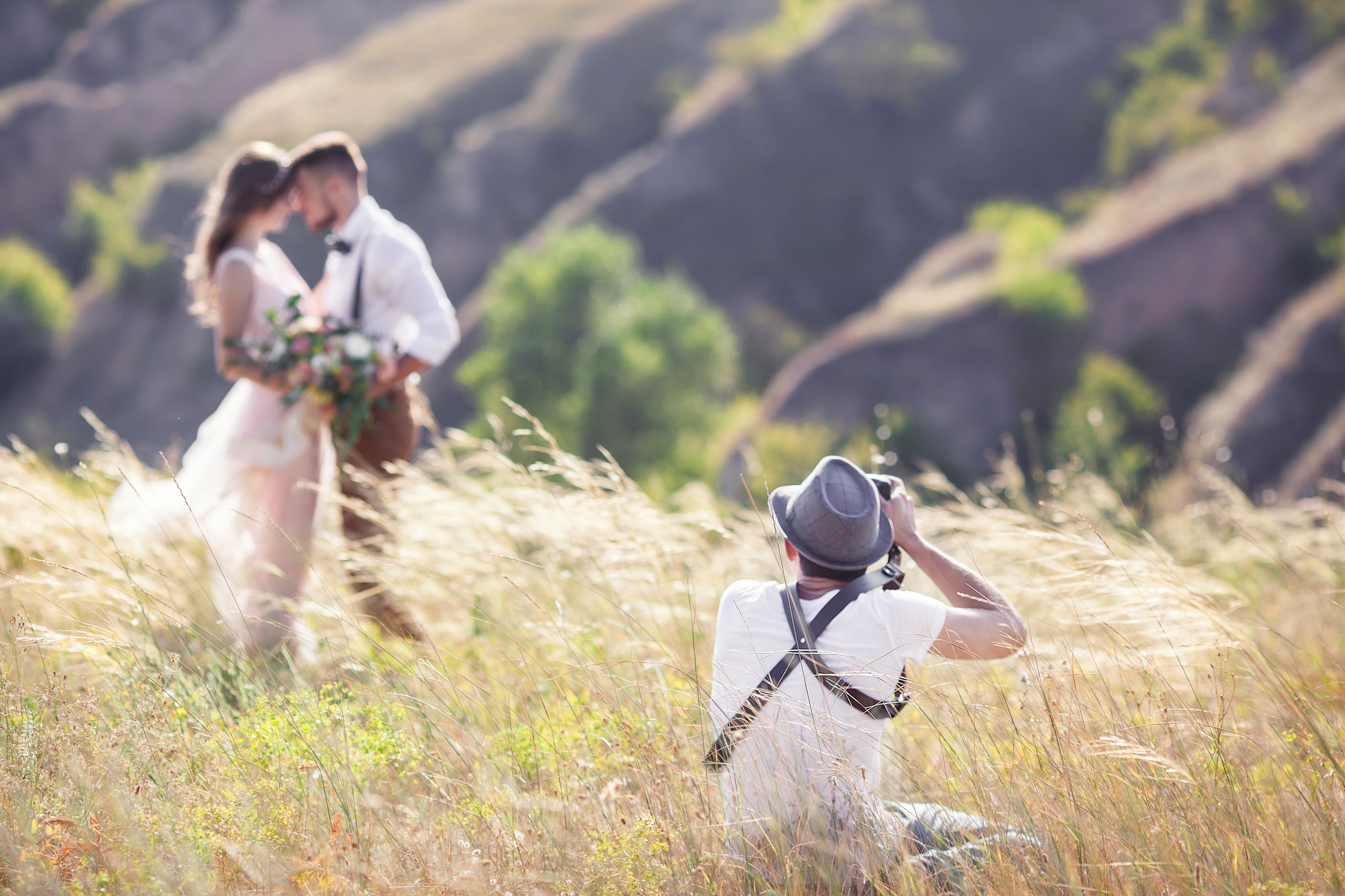 Photographer taking photo of bride and groom in a field.
