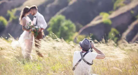 Photographer taking photo of bride and groom in a field.