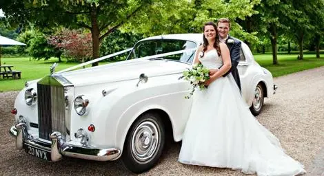 Bride and groom posing in front of beautiful white Rolls Royce