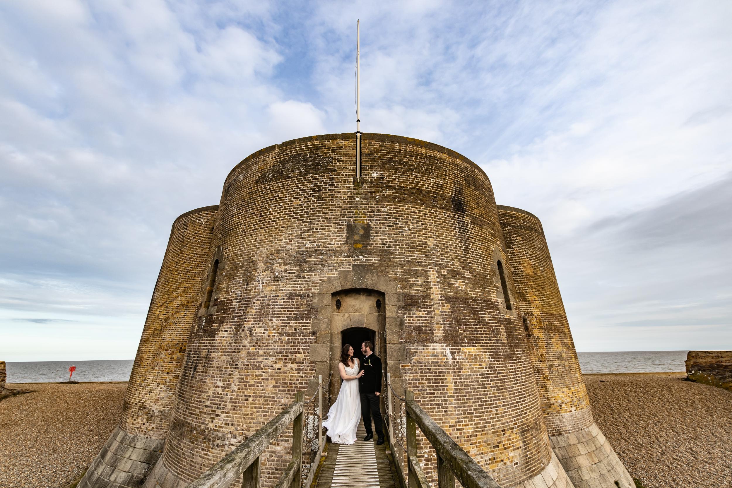 Bride and groom in front of a Martello Tower on the beach