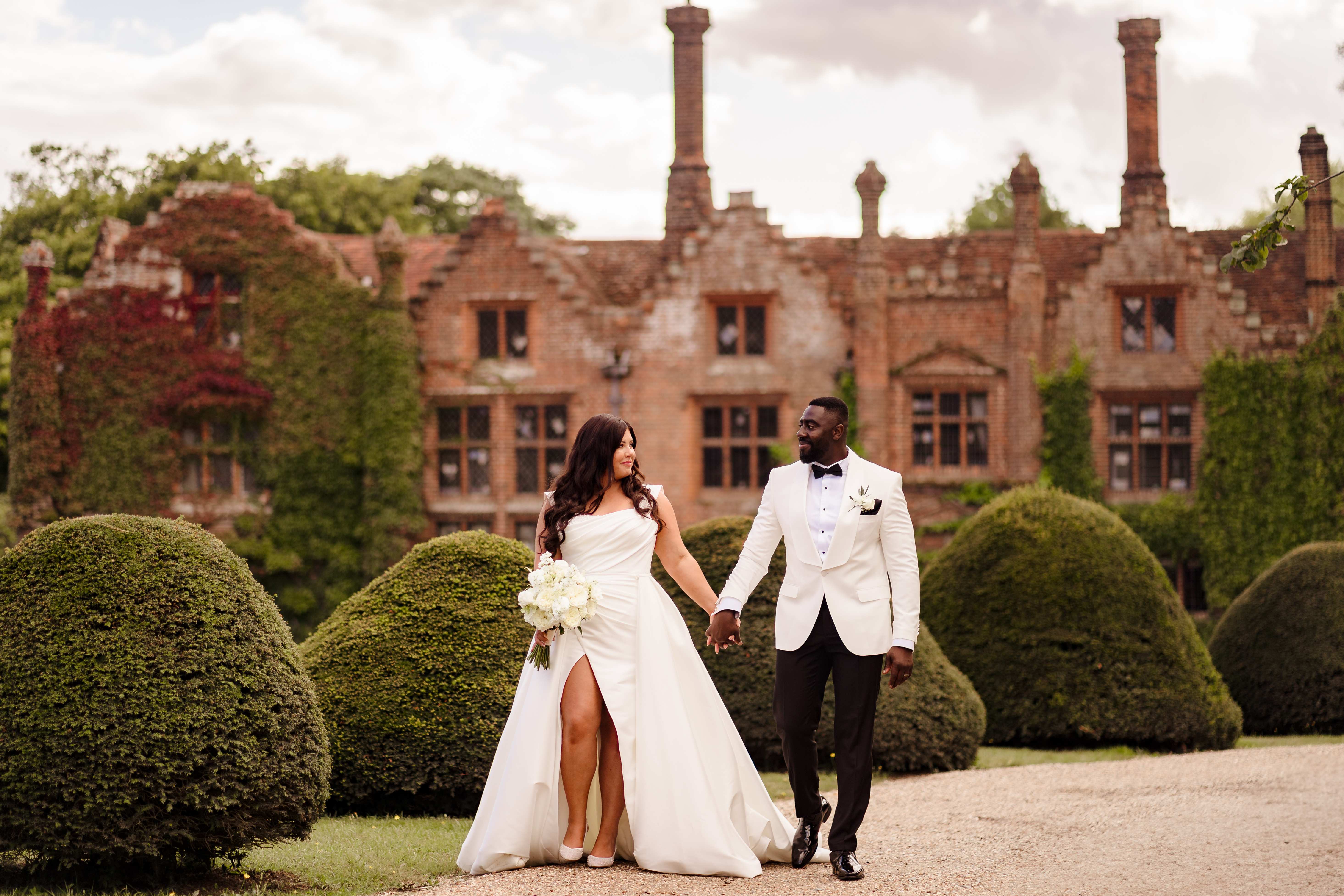 Bride and groom walking in manicured grounds with country house behind them