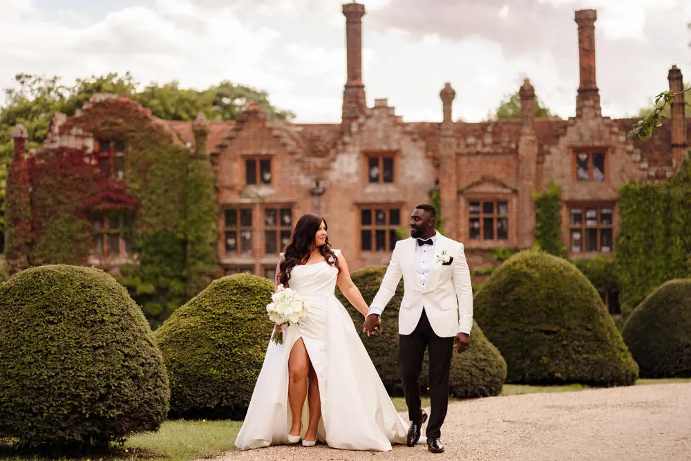 Bride and groom walking in manicured grounds with country house behind them