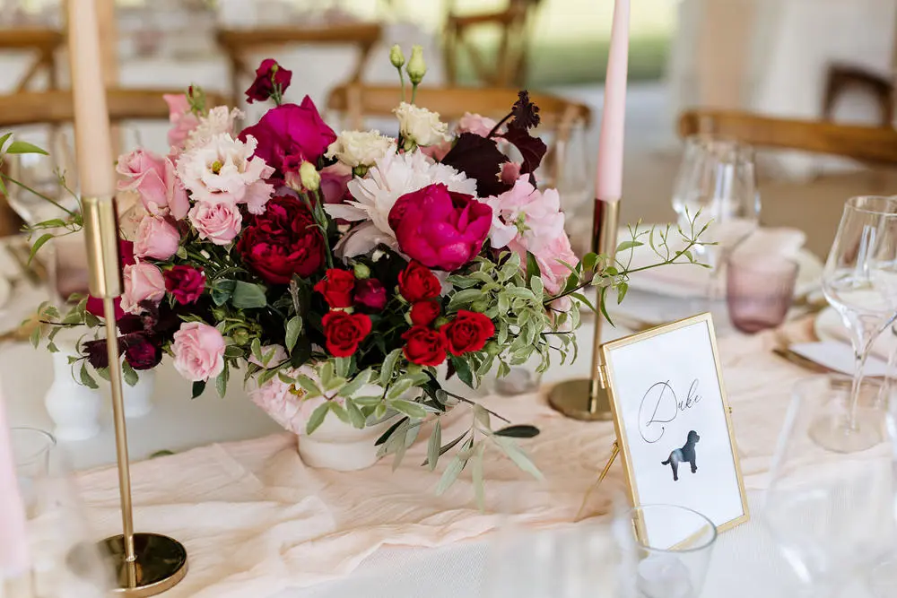 Beautifully laid wedding table with pink table cloth, bouquet of pink flowers and table name
