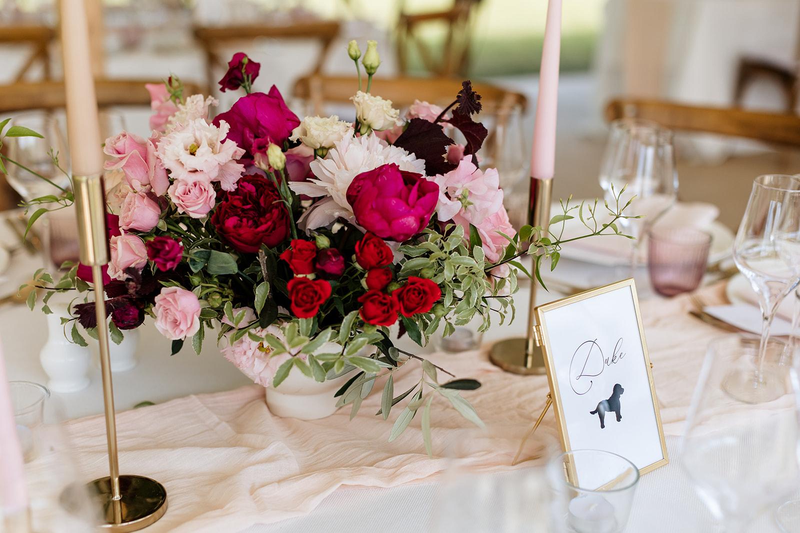 Beautifully laid wedding table with pink table cloth, bouquet of pink flowers and table name 