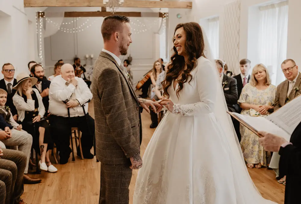 Bride and groom at ring exchange, smiling happily at each other
