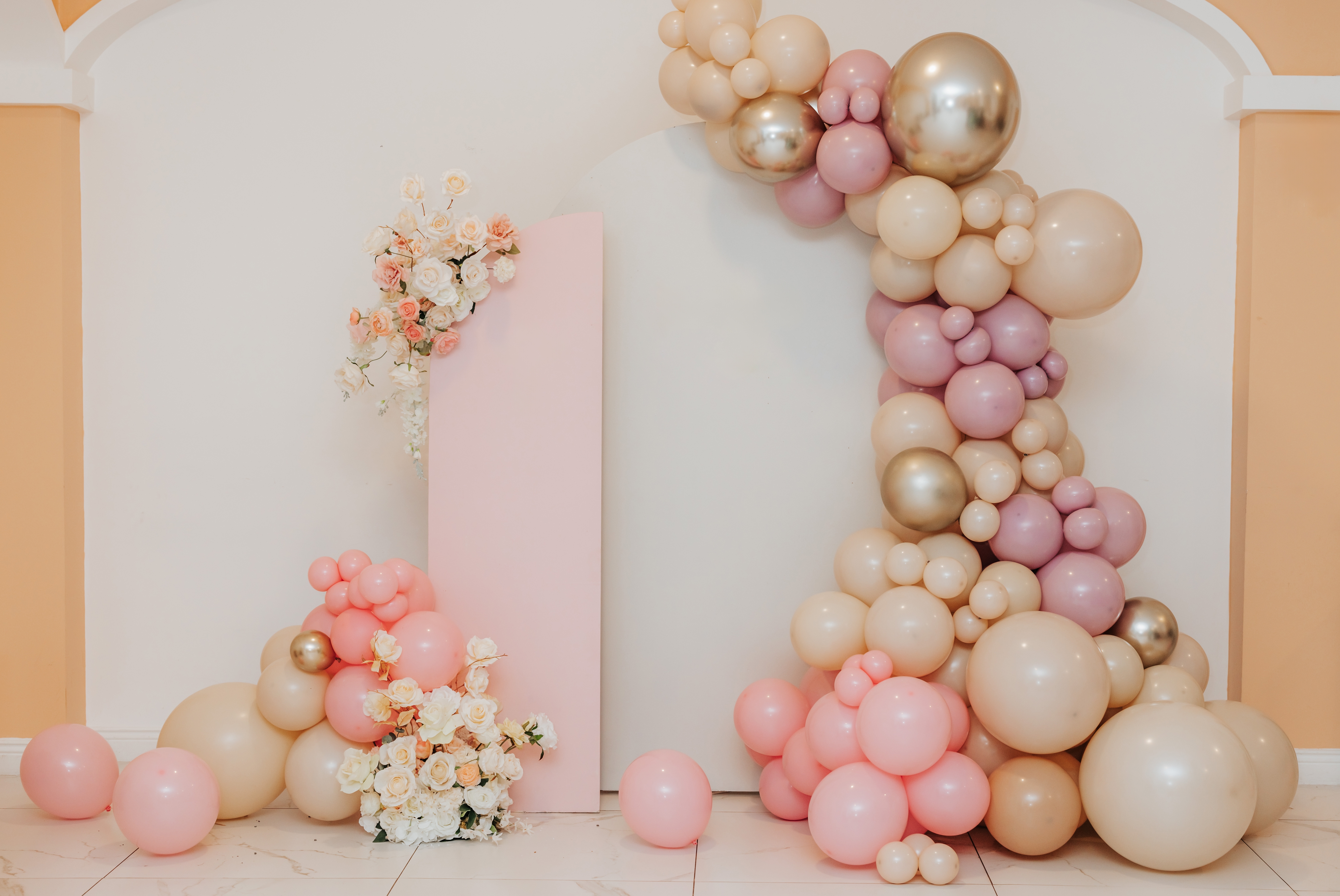 Balloon arch in pink, gold and white with further balloon and flower decorations around