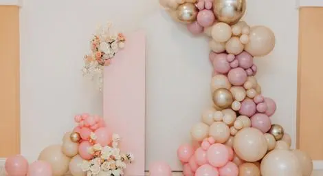 Balloon arch in pink, gold and white with further balloon and flower decorations around