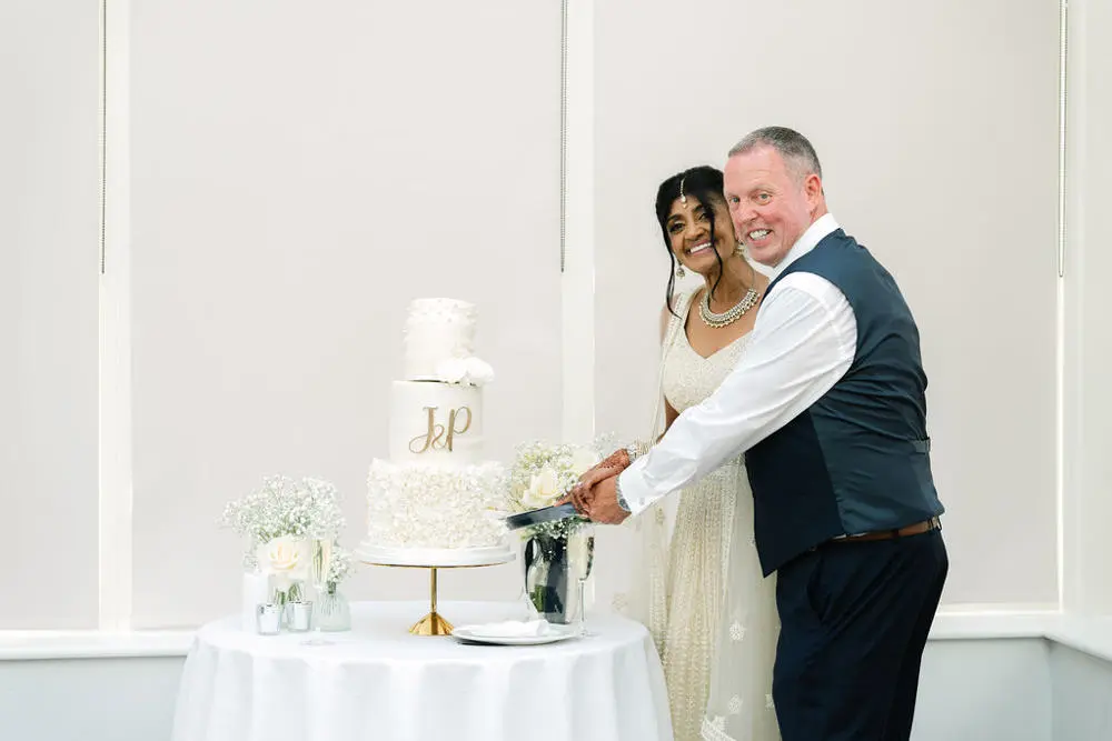 Bride and groom cutting three tier cake, smiling at camera