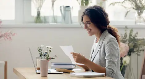 Young professional woman sitting at desk reading a piece of paper, smiling